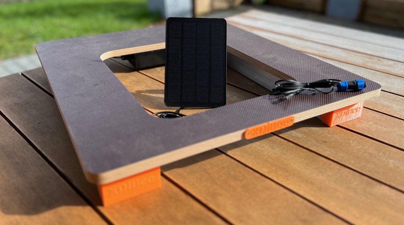 XDiBee Bienenstockwaage LTE: Holzrahmen mit orangen Füßen, Solarmodul und Anschlusskabel